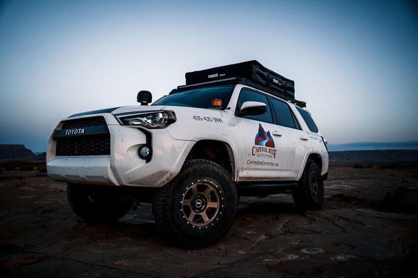 Un camion Toyota blanc, équipé d’un coffre de rangement sur le toit et arborant le logo de « Captive Reef » sur le côté. 3