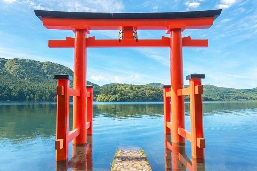 A red torii gate in a body of water with a forested hill in the background. 5