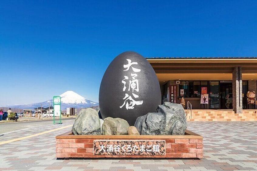 A large black spherical monument with Japanese characters, set on a brick platform with rocks, in front of a building with a clear blue sky and a mountain in the background. 1