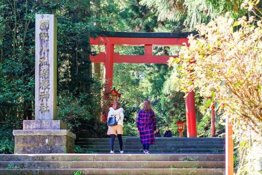 A stone monument, red torii gate, and a person in a plaid blanket at a shrine entrance. 5