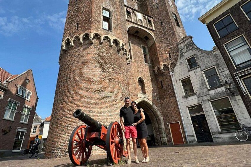 A historic brick tower with a cannon, a bicycle, and people standing in front. 5