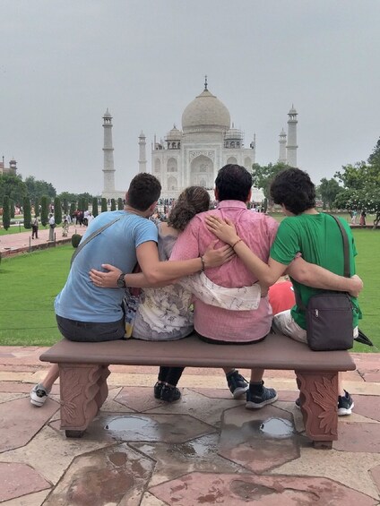 Vier Personen sitzen auf einer Bank und blicken auf den Taj Mahal. 4