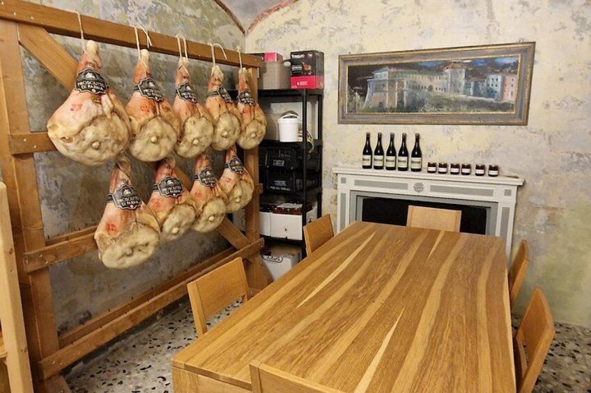 Un coin repas rustique avec une table en bois, de la viande suspendue et une cheminée ornée de bouteilles de vin. 2