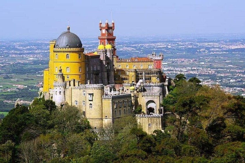 Pena Palace, a historic castle with yellow and red architecture, overlooking a city and lush greenery. 2