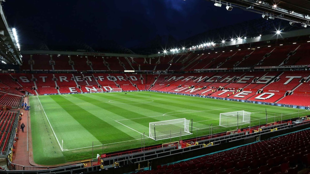 A large, empty stadium with red seats and a green field. 2