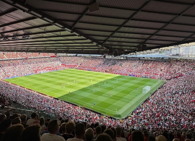 A large stadium filled with spectators, a football pitch, and a scoreboard. 1