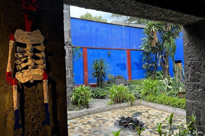 Uno scheletro, un muro azzurro e un giardino con piante e pavimento in pietra. 3