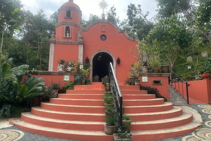A red church with a bell tower, surrounded by lush greenery and a patterned floor. 2