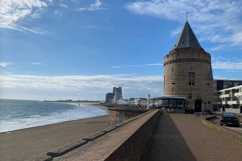A coastal promenade with a historic tower, beach, and modern buildings. 4
