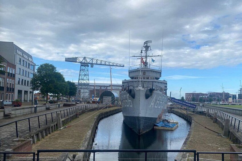A large ship docked in a canal with a crane and buildings in the background. 2