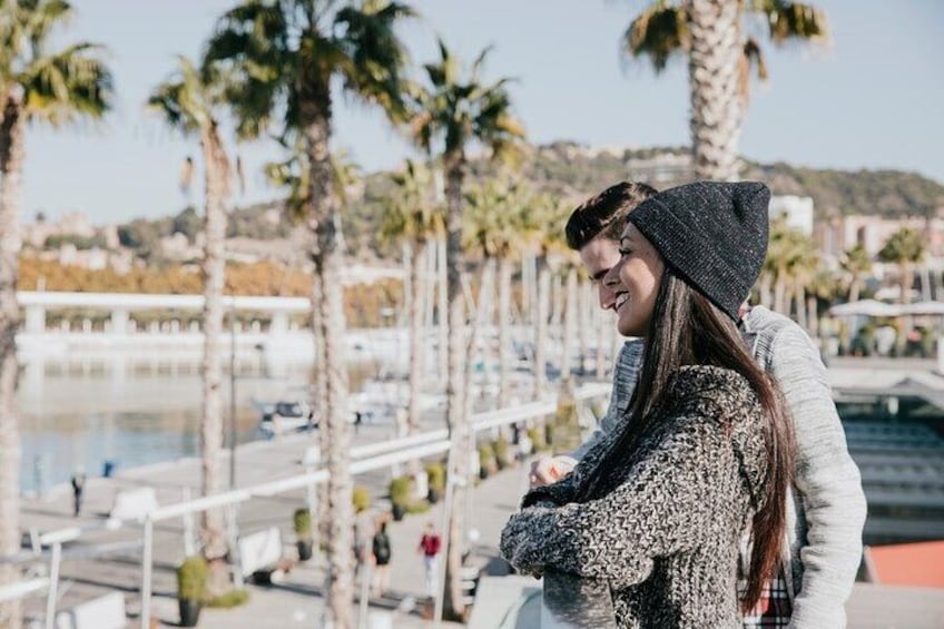 A couple standing by a waterfront with palm trees and a bridge in the background. 2