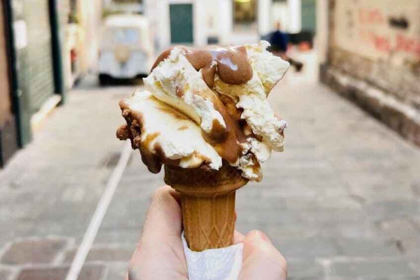 A hand holding a waffle cone with a scoop of ice cream topped with chocolate syrup. 3