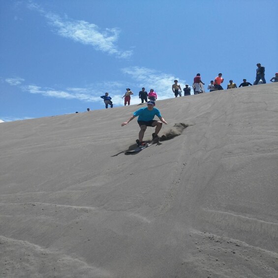 A person sliding down a sandy slope with others watching. 3