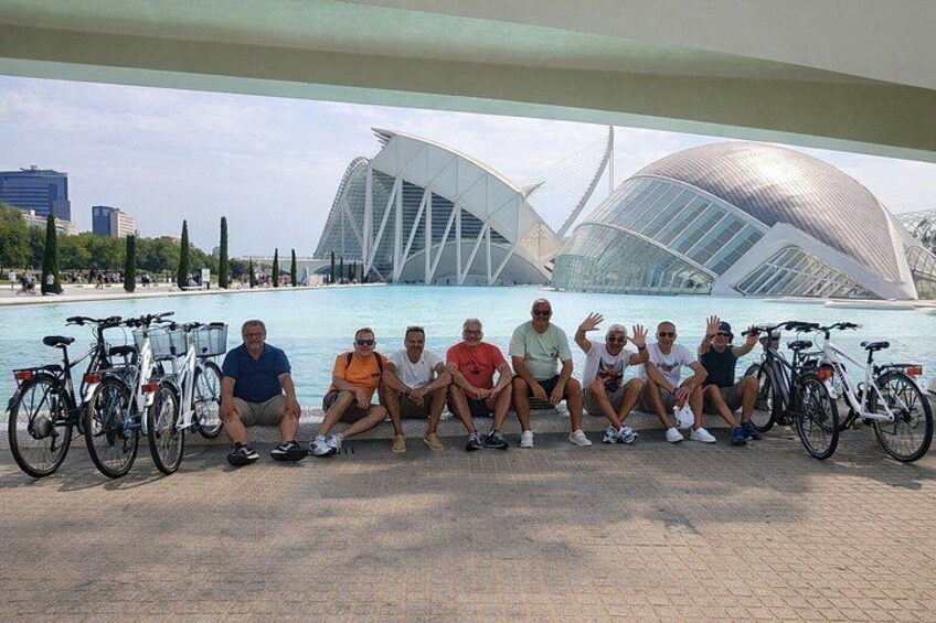 Un grupo de personas sentadas junto al agua, con una estructura arquitectónica moderna al fondo. 4