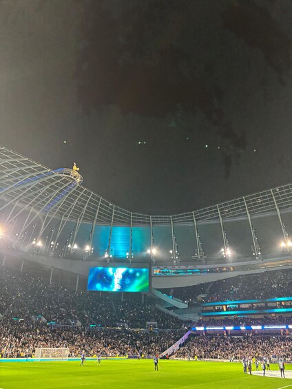 Un estadio grande con techo curvo, varias pantallas y una multitud de espectadores. 4