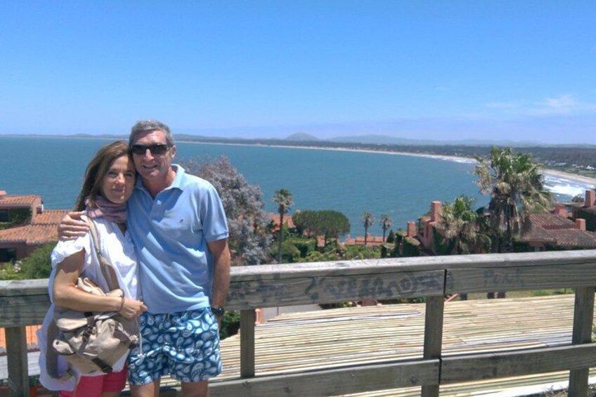 Una pareja está de pie en una terraza de madera con vistas a la costa, el océano y una cadena montañosa distante. 5