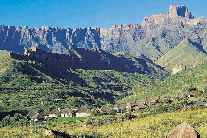 Eine gebirgige Landschaft mit Häusern an einem Hang und einem markanten Felsgipfel im Hintergrund. 4