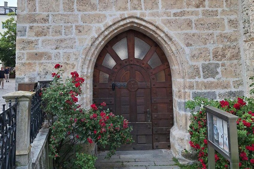 Un edificio in pietra con un'ampia porta di legno, fiori rossi e un muro di pietra. 4