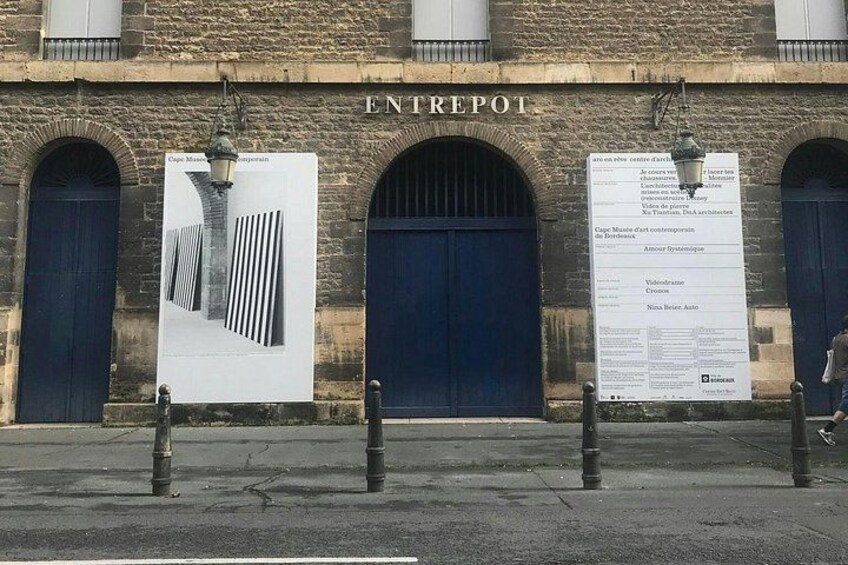 Een gebouw met de tekst 'ENTREPOT' boven de ingang, een grote poster op de muur, en paaltjes op de voorgrond. 5