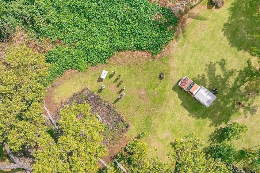 An aerial view of a green field with a small group of people, a parked vehicle, and a stone structure. 3