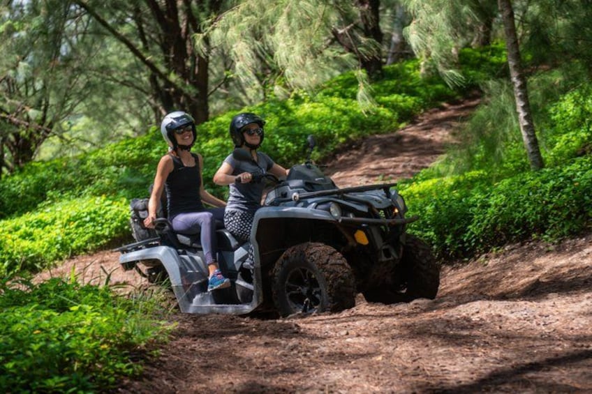 Two people riding an ATV on a dirt path in a forested area. 2
