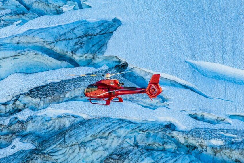 Un helicóptero rojo volando sobre un terreno montañoso nevado. 2