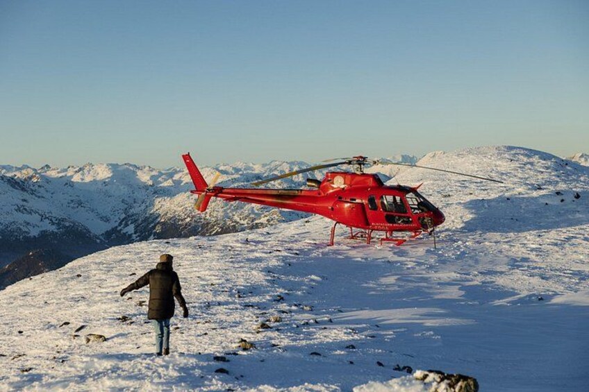A red helicopter on a snowy mountain with a person standing nearby. 4