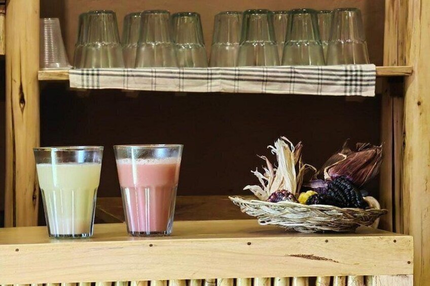 Two glasses of a yellowish beverage and a pinkish beverage on a wooden shelf. 2