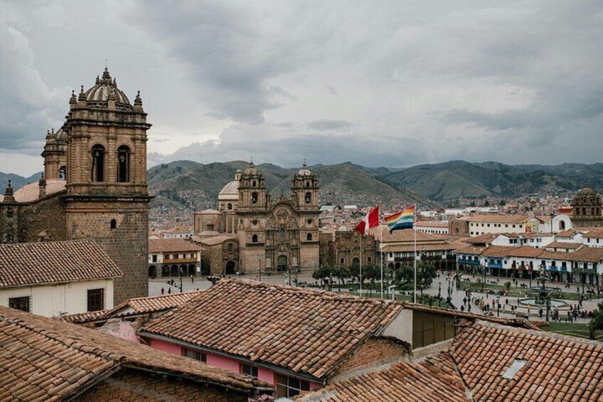 A historic cityscape with colonial architecture, including a prominent church with a bell tower, a plaza with people, and mountains in the background. 3