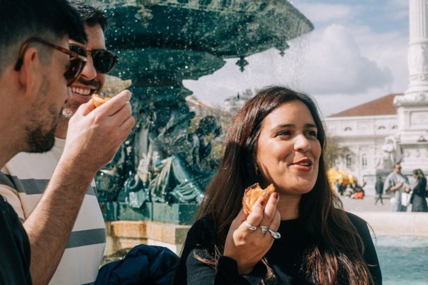 A couple eating near a fountain with a historical building in the background. 3
