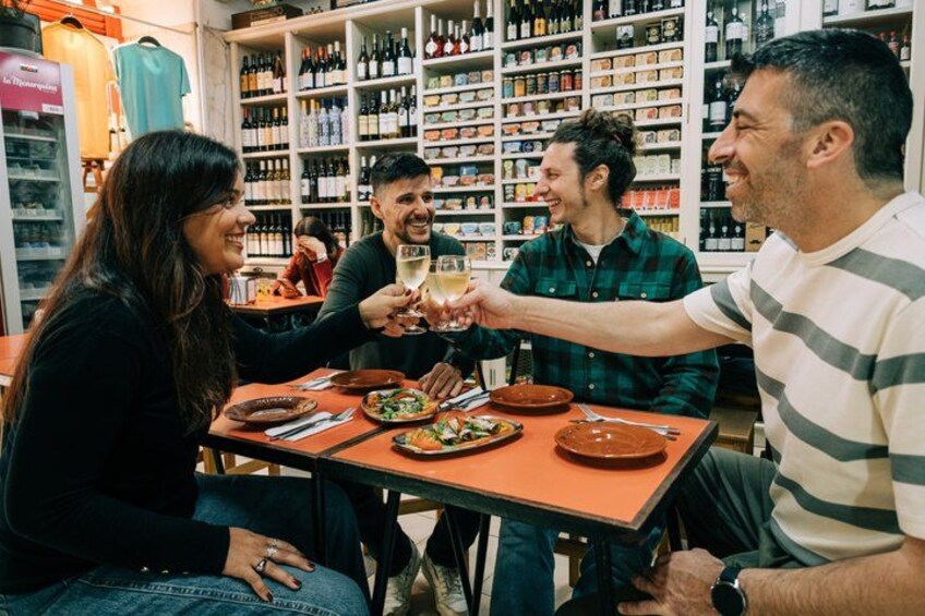 A group of people toasting with wine glasses at a table in a wine shop. 5