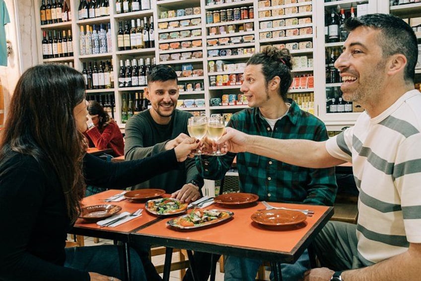 A group of people toasting with drinks at a table in a restaurant with shelves of bottles in the background. 4