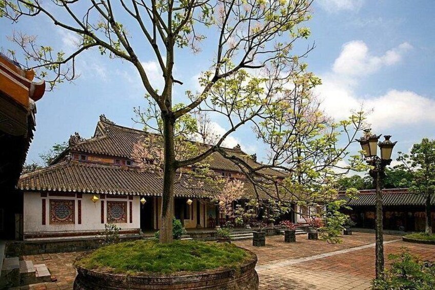Un patio tradicional con un edificio de techo de tejas, un árbol grande y un farol de piedra. 3