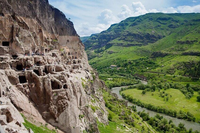 A cliff with ancient rock dwellings, a river, and a green valley. 2