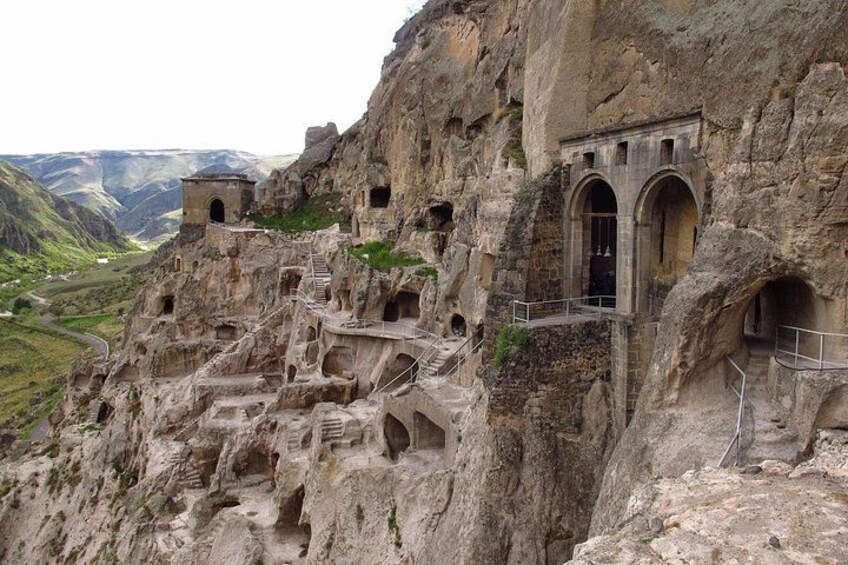 A rugged cliffside with ancient rock-cut architecture, including arched doorways and a staircase. 3