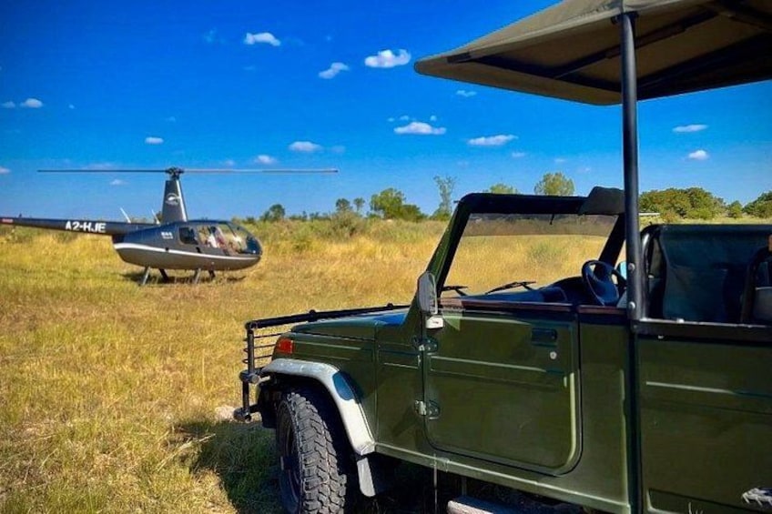 A green off-road vehicle parked in a grassy field with a helicopter in the background. 4