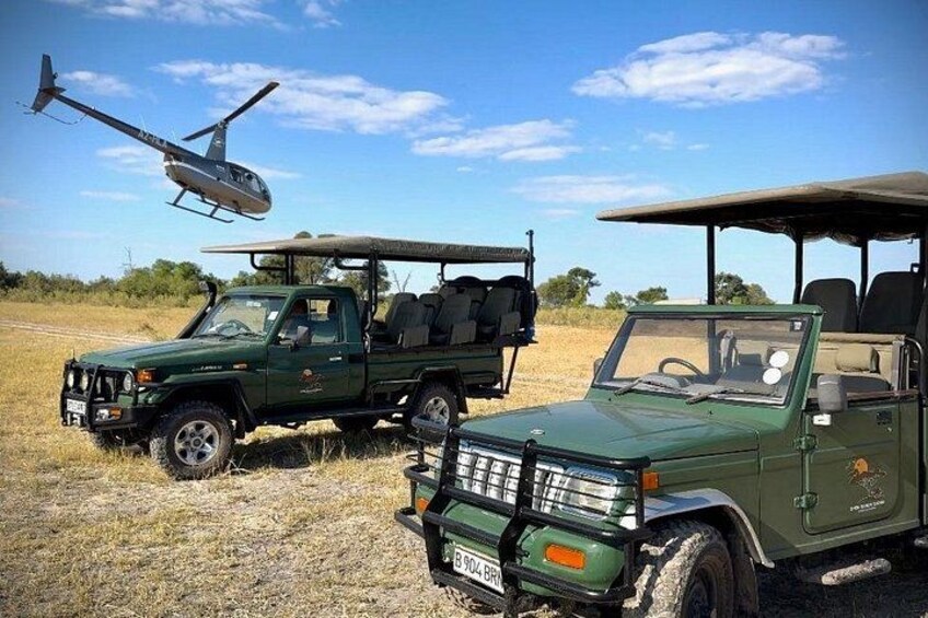 Un vehículo todoterreno verde con un portaequipajes y una lona, estacionado en un campo, con un helicóptero al fondo. 3