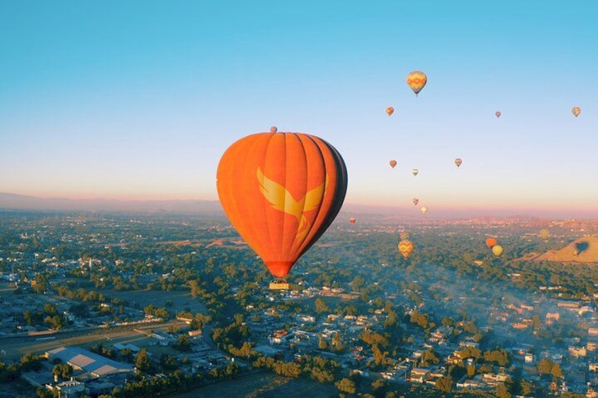 A hot air balloon over a cityscape with multiple balloons in the sky. 5