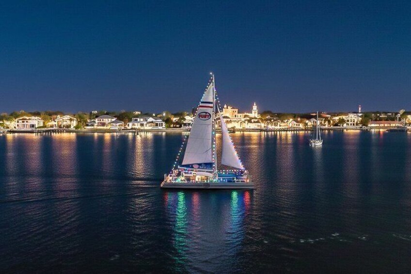A sailboat with a white hull and blue accents sailing on a calm body of water at night. 1