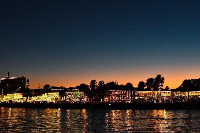 A waterfront cityscape at dusk with illuminated buildings and a calm river reflecting the lights. 4