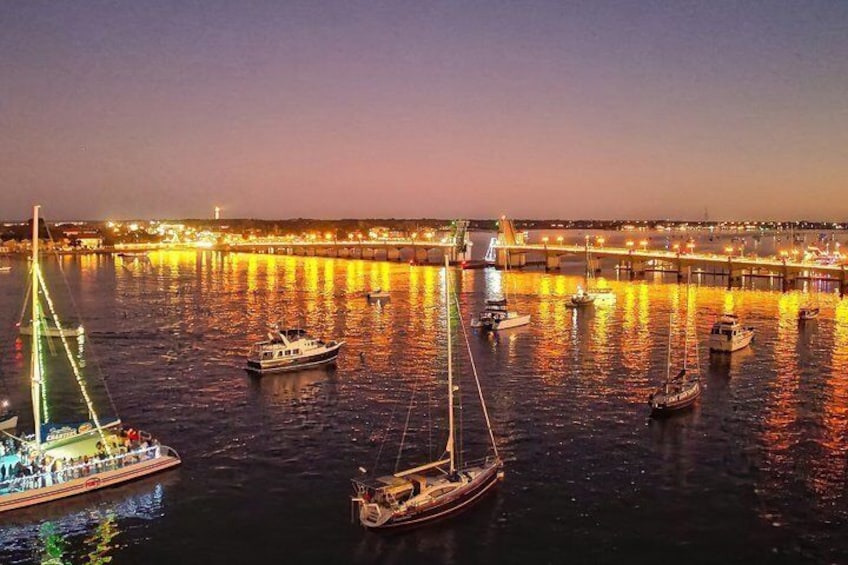 A river with boats, a bridge, and city lights at dusk. 2