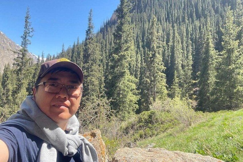 A person taking a selfie with a mountainous forest background. 4