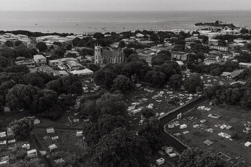 An aerial view of a coastal town with a prominent church, dense tree coverage, and a cemetery. 2