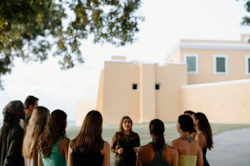 A group of people standing outdoors, facing a building with a flat roof and rectangular windows. 1