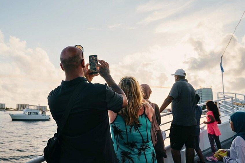 Un grupo de personas en un barco, algunas tomando fotos, con un horizonte urbano y un puente al fondo. 5