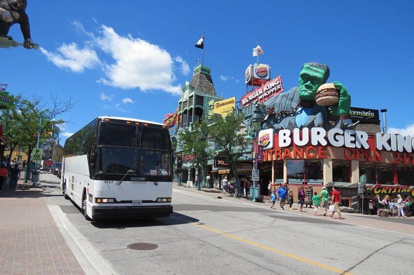 A city street with a large bus, Burger King, and a statue of a figure holding a burger. 3