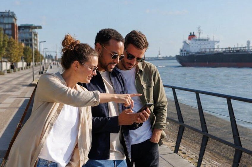 Drei Personen stehen am Ufer und betrachten ein Smartphone. 1