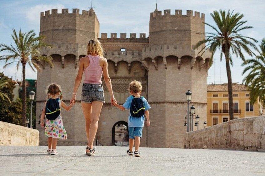 A woman and two children walking on a paved path towards a historic castle with towers. 1