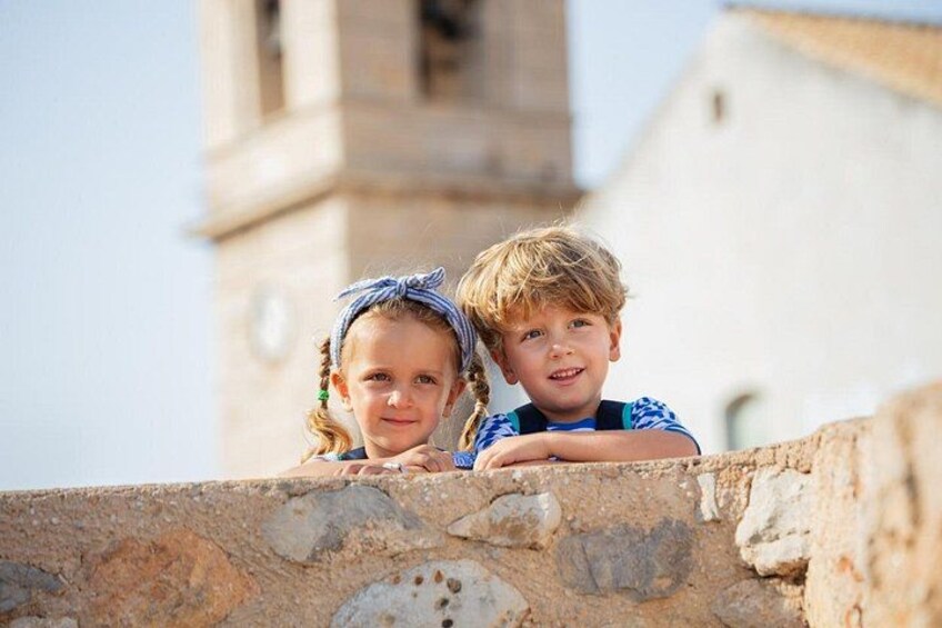 Two children leaning on a stone wall with a church tower in the background. 3