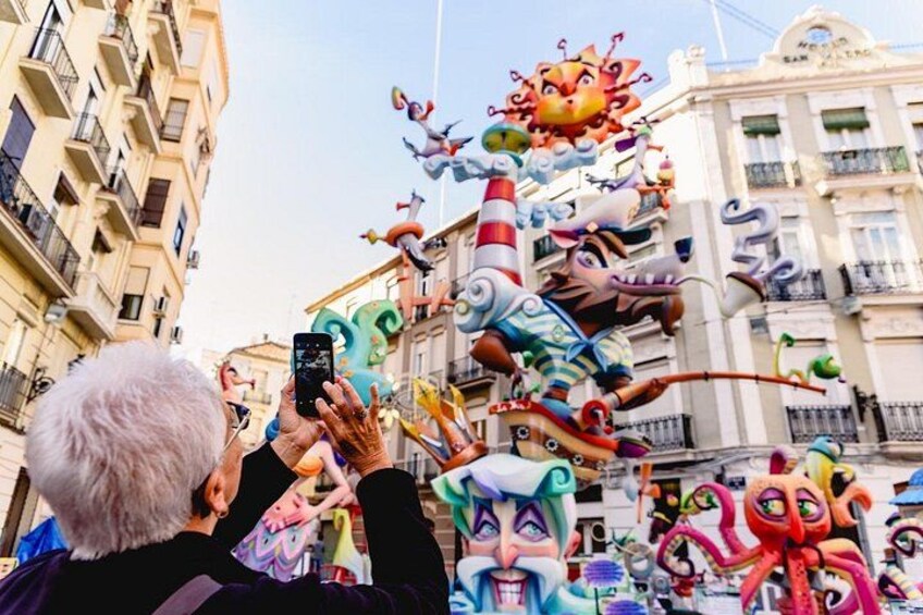 A person taking a photo of a colorful street decoration with various whimsical figures. 2